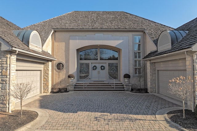 doorway to property featuring decorative driveway, french doors, stone siding, and an attached garage