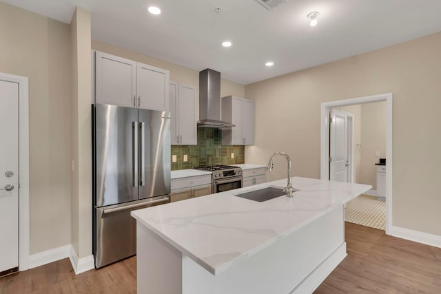 kitchen with light wood finished floors, tasteful backsplash, wall chimney exhaust hood, stainless steel appliances, and a sink