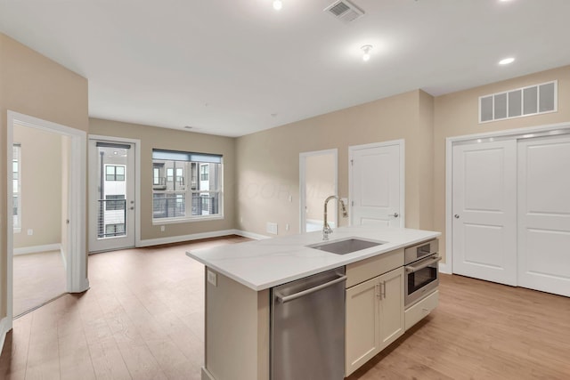 kitchen with a center island with sink, visible vents, stainless steel appliances, light wood-style floors, and a sink