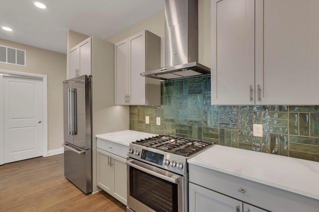 kitchen featuring wall chimney range hood, visible vents, appliances with stainless steel finishes, and light countertops