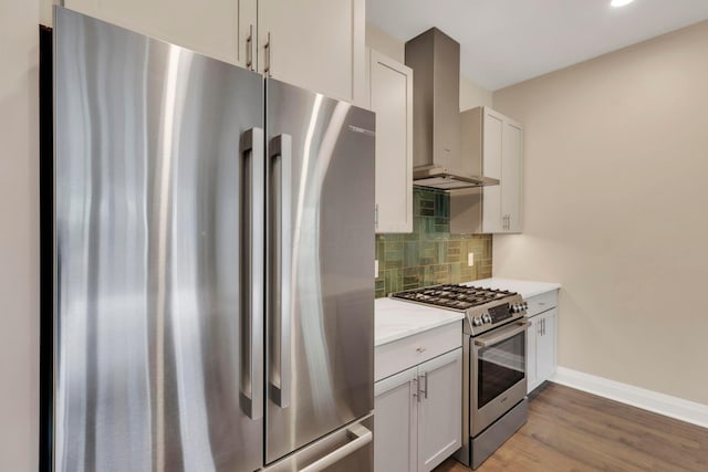 kitchen featuring tasteful backsplash, wall chimney exhaust hood, appliances with stainless steel finishes, wood finished floors, and light countertops