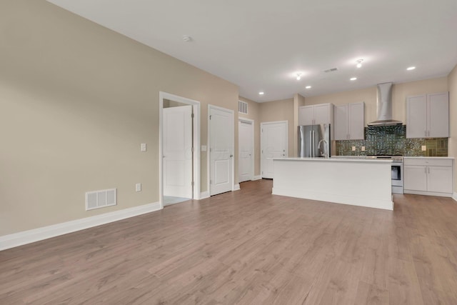 kitchen with stainless steel appliances, tasteful backsplash, visible vents, light wood-style floors, and wall chimney exhaust hood