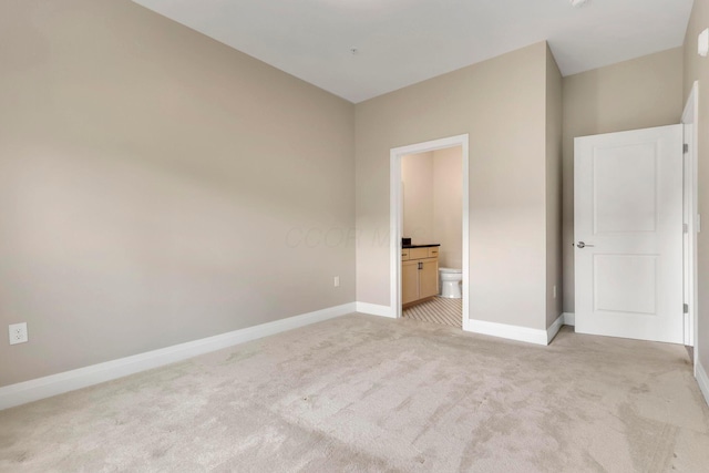 unfurnished bedroom featuring light carpet, ensuite bathroom, and baseboards