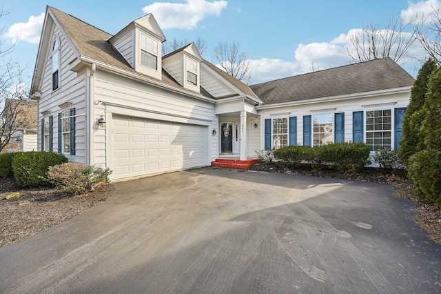 new england style home featuring driveway, an attached garage, and roof with shingles