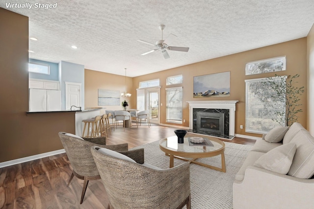 living room featuring a textured ceiling, baseboards, wood finished floors, and a high end fireplace