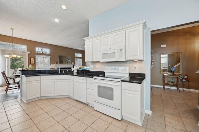 kitchen with white appliances, light tile patterned floors, dark countertops, a peninsula, and a notable chandelier