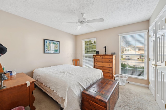 bedroom featuring light carpet, a textured ceiling, multiple windows, and a ceiling fan