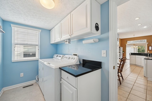 laundry room with cabinet space, light tile patterned flooring, a textured ceiling, and washing machine and clothes dryer