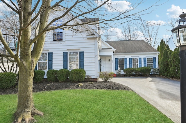 view of front of house featuring roof with shingles, driveway, and a front lawn