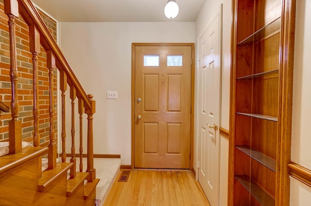 foyer entrance with stairs, brick wall, light wood-style flooring, and baseboards