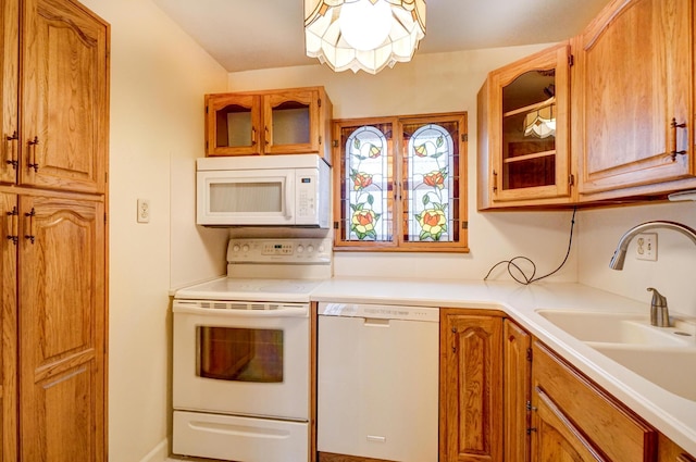 kitchen featuring white appliances, a sink, light countertops, brown cabinetry, and glass insert cabinets