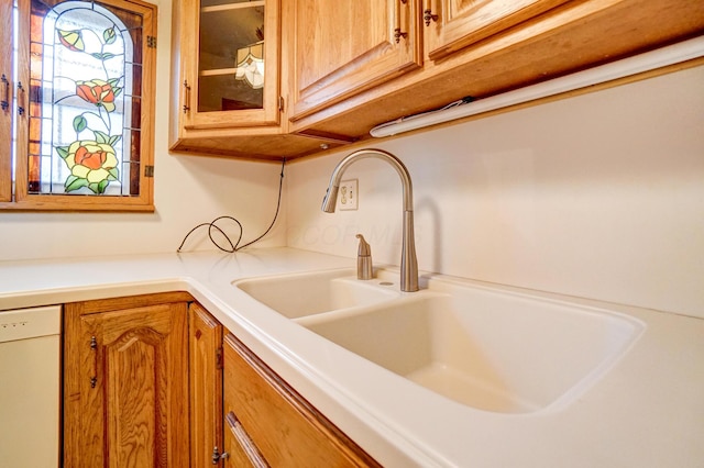 interior details with white dishwasher, a sink, light countertops, brown cabinets, and glass insert cabinets