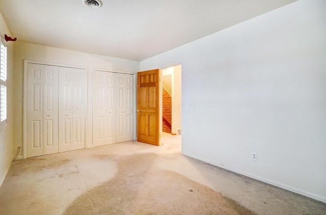 unfurnished bedroom featuring carpet, visible vents, and two closets