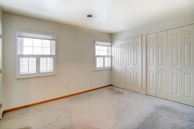 unfurnished bedroom featuring baseboards, carpet flooring, visible vents, and multiple closets