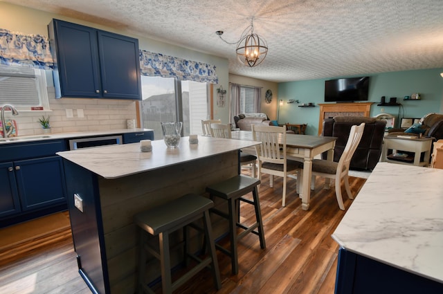 kitchen with dark wood-style floors, open floor plan, a sink, blue cabinets, and a kitchen breakfast bar