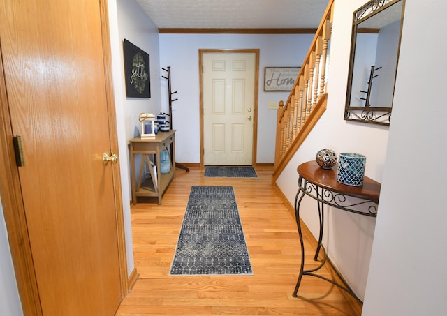 interior space featuring crown molding, a textured ceiling, wood finished floors, baseboards, and stairs