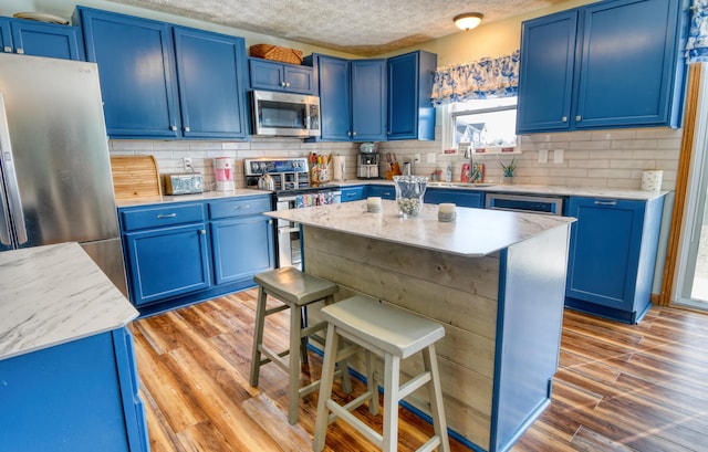 kitchen with stainless steel appliances, light wood finished floors, backsplash, and blue cabinets