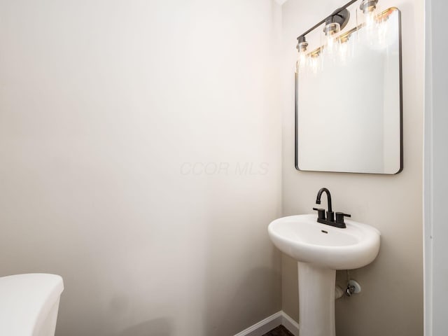 half bathroom featuring toilet, baseboards, and a sink