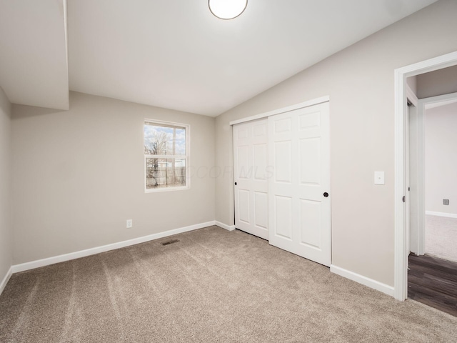 unfurnished bedroom with lofted ceiling, a closet, visible vents, carpet flooring, and baseboards