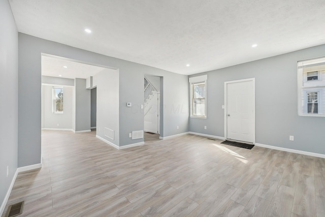 unfurnished living room with light wood-type flooring, visible vents, baseboards, and stairway