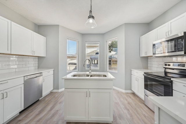 kitchen featuring decorative light fixtures, decorative backsplash, light wood-style flooring, stainless steel appliances, and a sink