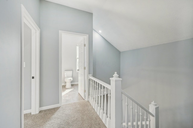 hall featuring carpet, lofted ceiling, an upstairs landing, and baseboards