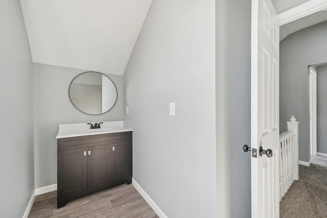 bathroom with baseboards, wood finished floors, vanity, and vaulted ceiling