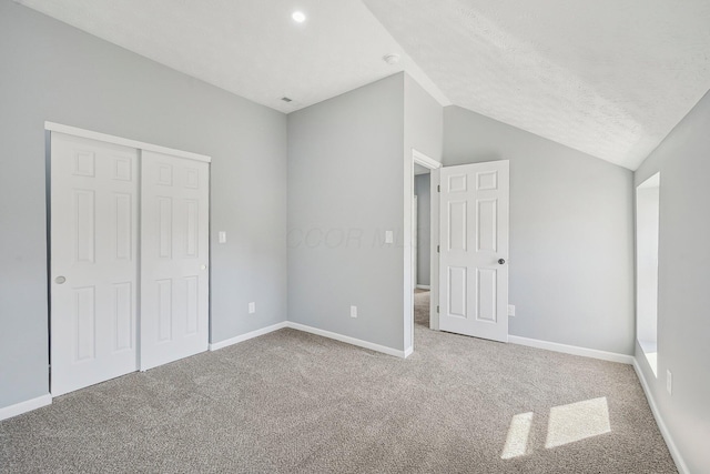 unfurnished bedroom featuring baseboards, carpet floors, a closet, and vaulted ceiling