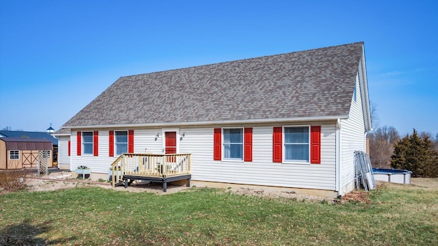 view of front of house with a shed, roof with shingles, an outdoor structure, a front yard, and a wooden deck