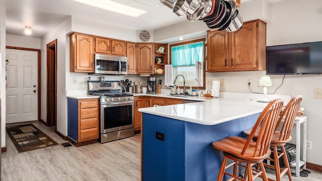 kitchen with light wood-style flooring, stainless steel appliances, a peninsula, a breakfast bar area, and light countertops