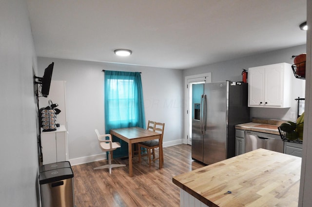 kitchen featuring butcher block countertops, wood finished floors, baseboards, white cabinets, and appliances with stainless steel finishes