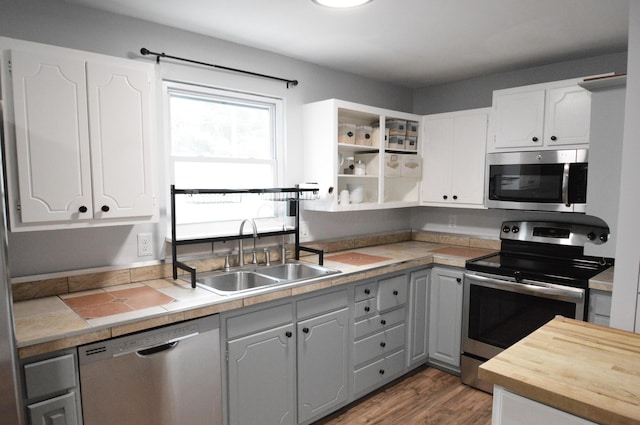 kitchen with stainless steel appliances, wood finished floors, a sink, white cabinetry, and open shelves