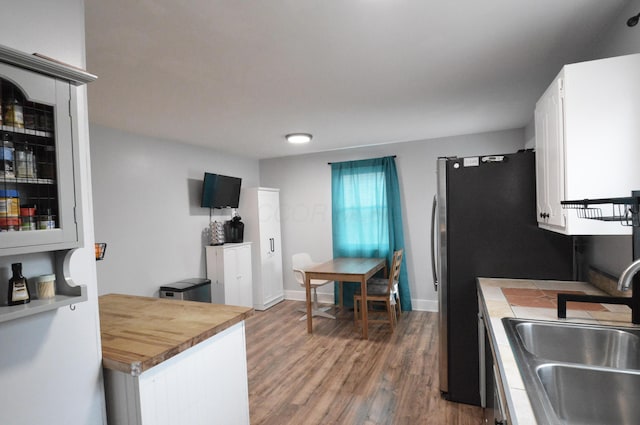 kitchen featuring baseboards, tile counters, white cabinets, wood finished floors, and a sink