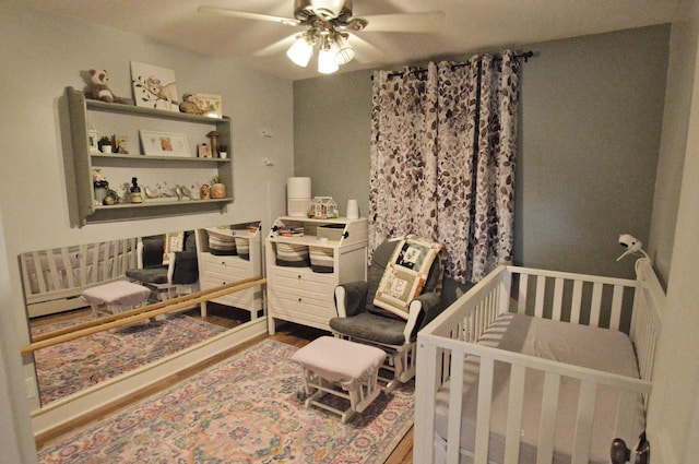 bedroom with a ceiling fan, dark wood-style flooring, and a crib