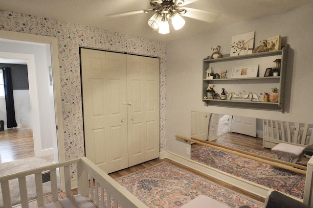 bedroom featuring ceiling fan, a closet, wood finished floors, and wallpapered walls