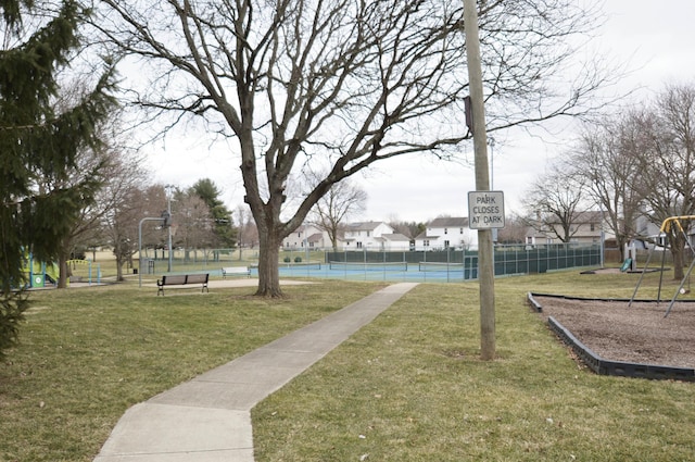 view of community featuring a tennis court, fence, playground community, and a yard