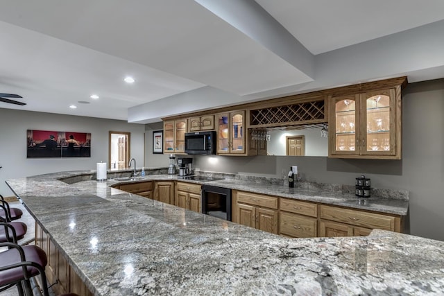 kitchen with beverage cooler, light stone countertops, black appliances, a peninsula, and glass insert cabinets