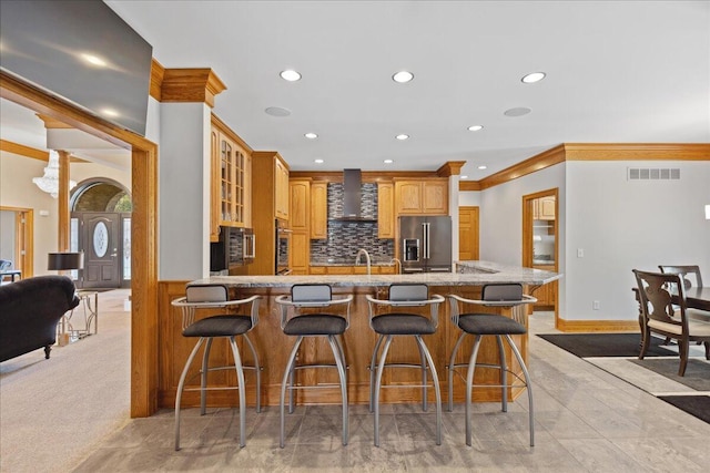 kitchen featuring recessed lighting, stainless steel appliances, light stone counters, wall chimney range hood, and a peninsula
