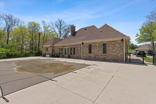 rear view of property with a chimney, brick siding, fence, a fenced in pool, and a patio
