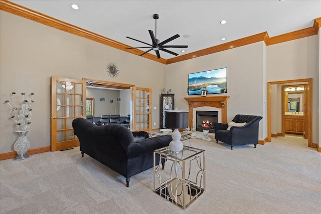 living room featuring carpet flooring, a glass covered fireplace, baseboards, a ceiling fan, and crown molding