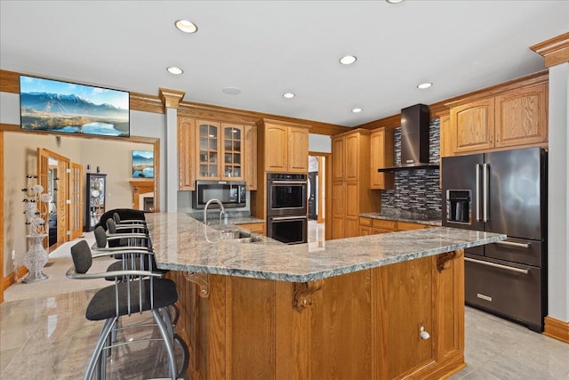 kitchen with recessed lighting, appliances with stainless steel finishes, wall chimney range hood, a sink, and a kitchen breakfast bar