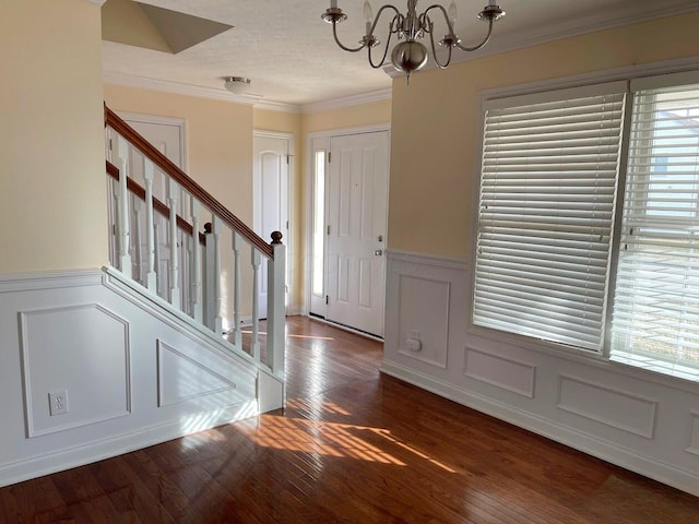 foyer featuring a notable chandelier, a decorative wall, ornamental molding, hardwood / wood-style floors, and stairs