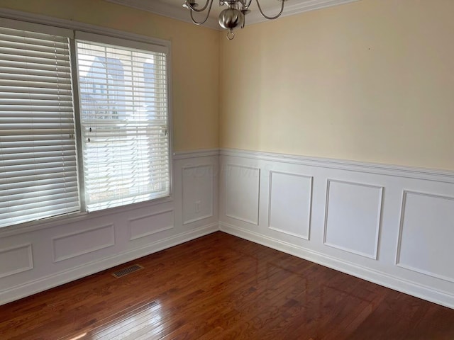 spare room featuring an inviting chandelier, dark wood finished floors, visible vents, and a healthy amount of sunlight