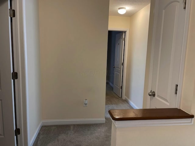 hall with a textured ceiling, carpet floors, and baseboards