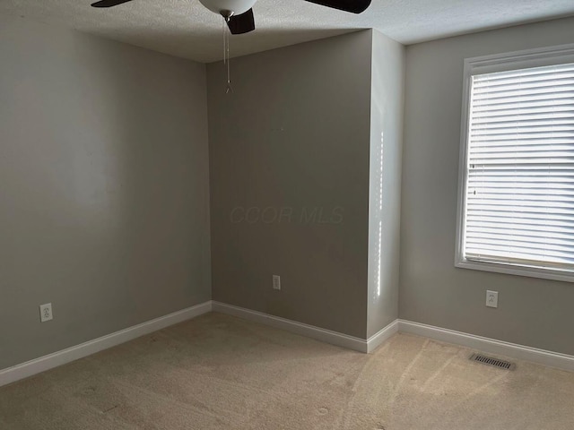 unfurnished room with a textured ceiling, light colored carpet, a ceiling fan, baseboards, and visible vents