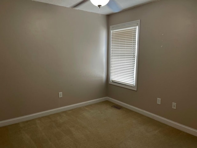 empty room featuring a ceiling fan, visible vents, light carpet, and baseboards