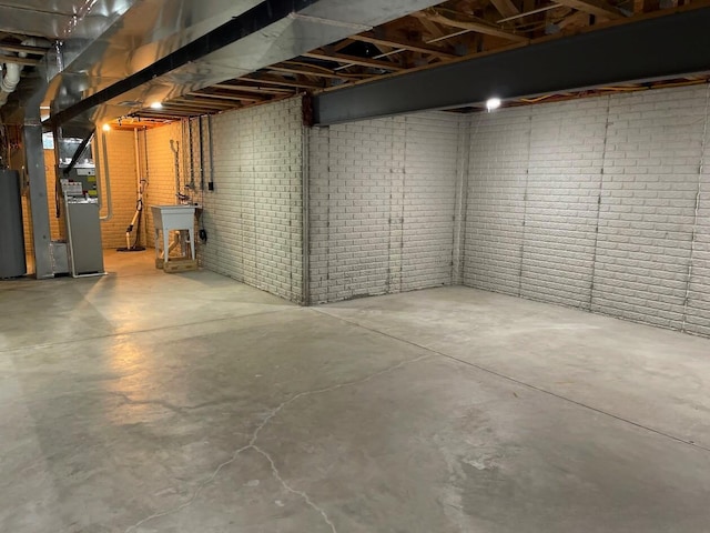 unfinished basement with heating unit, water heater, a sink, and brick wall