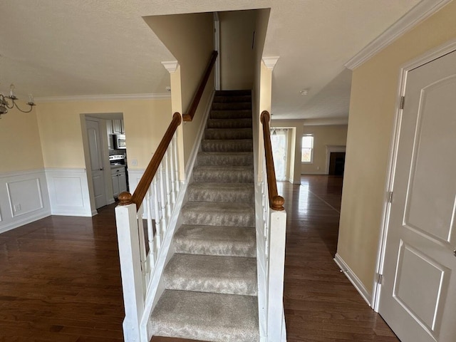 staircase with a wainscoted wall, crown molding, a fireplace, and wood finished floors