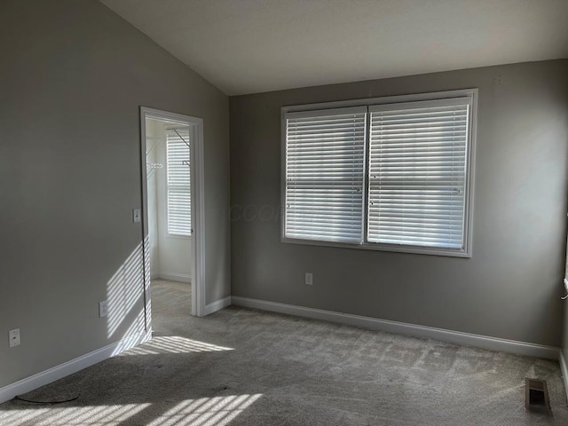 empty room with carpet floors, visible vents, baseboards, and vaulted ceiling