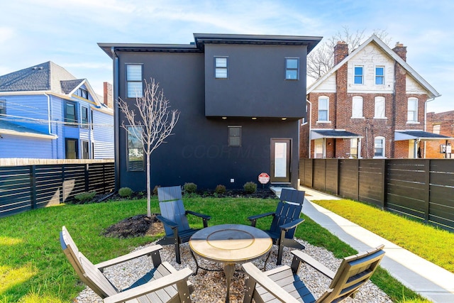 rear view of property with a fenced backyard, a yard, a fire pit, and stucco siding